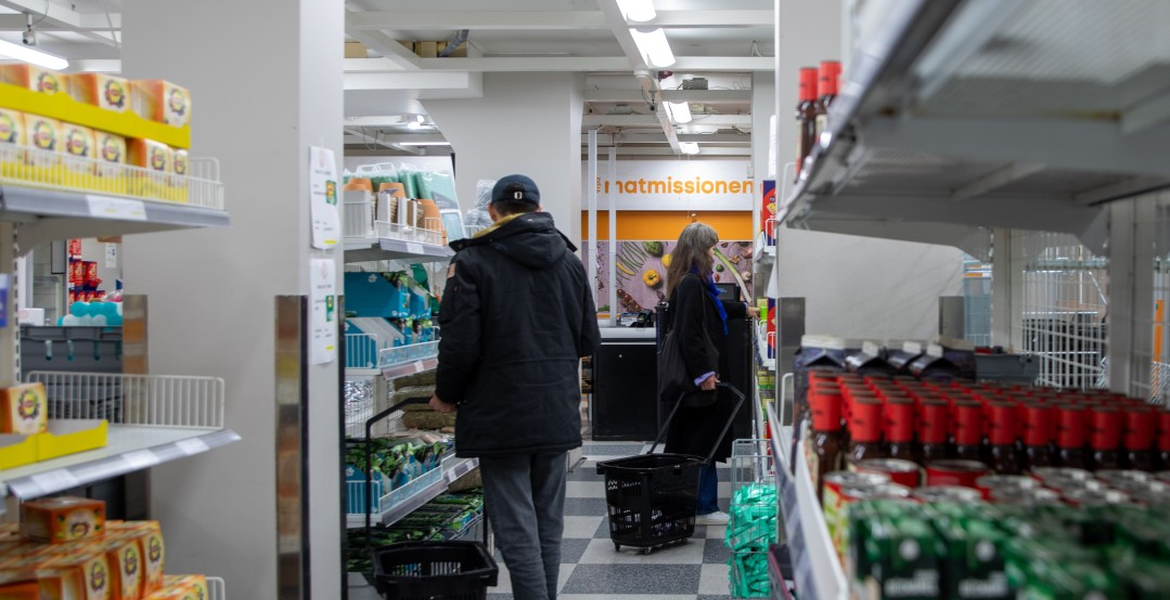 Ostajia vetokorien kanssa ruokakaupan käytävällä, taustalla Matmissionen-kyltti.