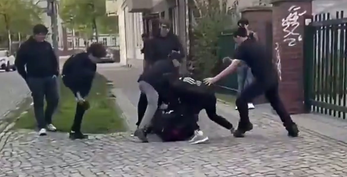 Videokuva, jossa ryhmä nuoria piirittää poikaa jalkakäytävällä metalliaidan vieressä raportoidun pahoinpitelyn aikana